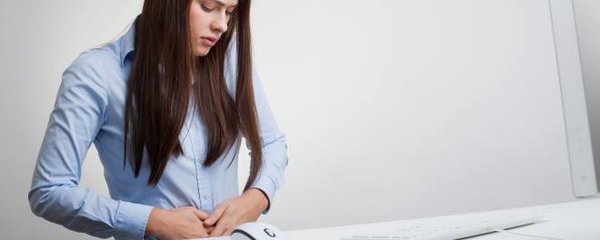 Frau mit Magenkrämpfen am Arbeitsplatz