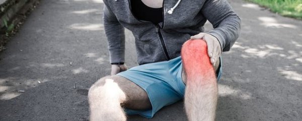 Läufer sitzt mit geschwollenem Knie auf dem Boden